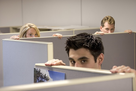 Office with cubicles, with three employees peering over the top of the cubicle walls with worried faces